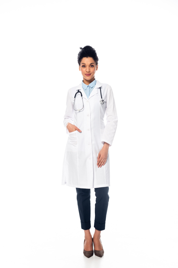 Вид спереди на африканского американского врача со стетоскопом и рукой в кармане, улыбающегося на белом фоне
 - Фото, изображение