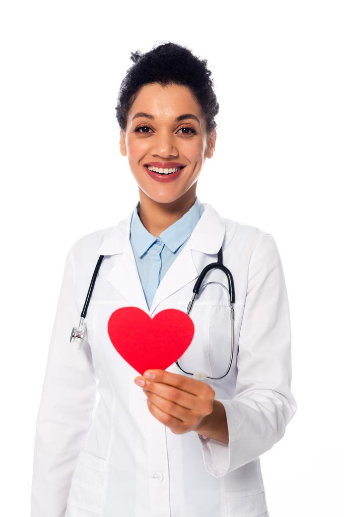 Frontansicht eines afrikanisch-amerikanischen Arztes mit Stethoskop, das ein dekoratives rotes Herz isoliert auf weiß zeigt - Foto, Bild