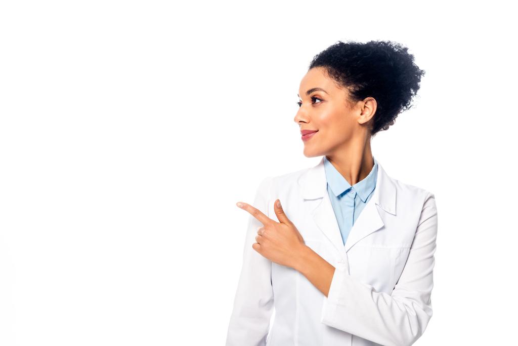 Μπροστά όψη του Αφροαμερικανού γιατρού χαμογελώντας και δείχνοντας στην άκρη απομονωμένο στο λευκό - Φωτογραφία, εικόνα