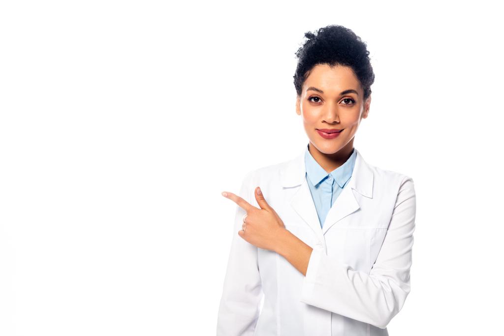 Frontansicht eines afrikanisch-amerikanischen Arztes, der in die Kamera blickt, lächelt und mit dem Finger auf Weiß zeigt - Foto, Bild
