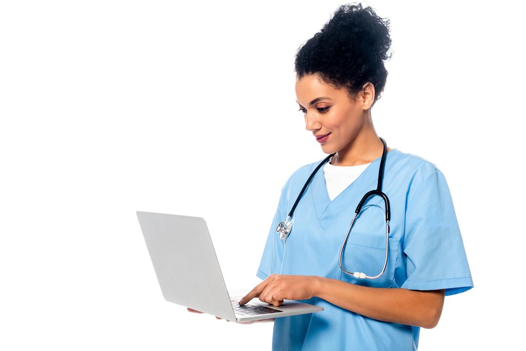 Enfermera afroamericana con estetoscopio enfocada en el uso de laptop aislado en blanco
 - Foto, Imagen