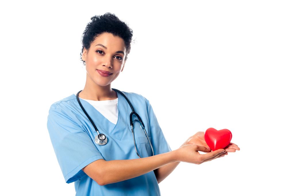 Африканская американская медсестра со стетоскопом показывает декоративное красное сердце, смотрящее на камеру, изолированную на белом
 - Фото, изображение