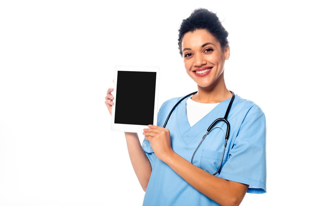 African american nurse looking at camera, smiling and showing digital tablet isolated on white - Fotografie, Obrázek