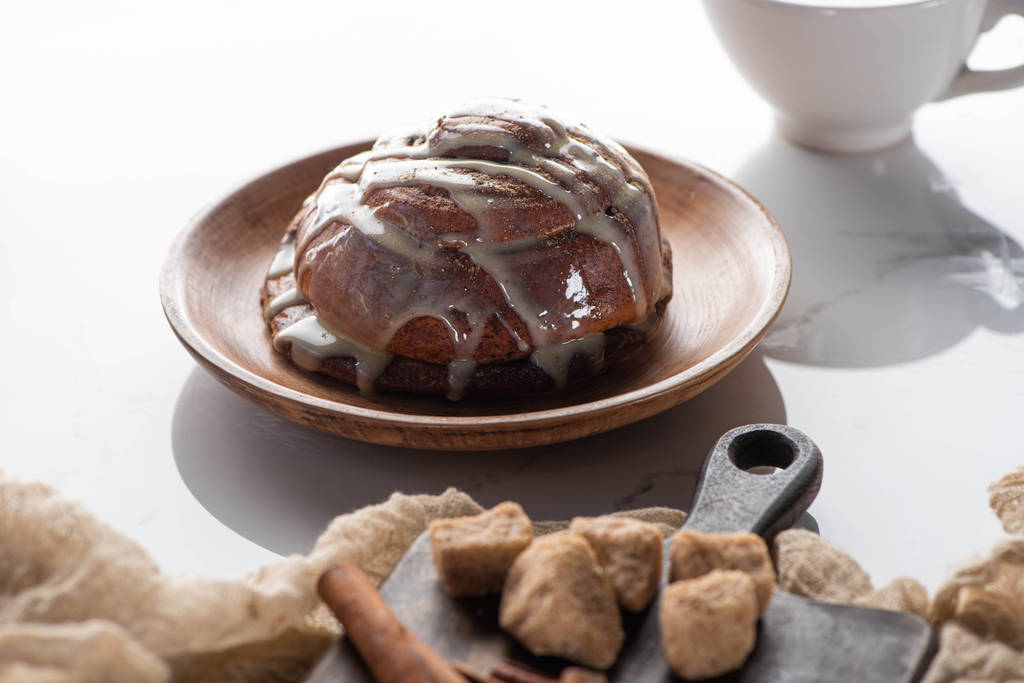 selective focus of fresh homemade cinnamon roll on plate near cutting board with brown sugar and cinnamon - Photo, Image