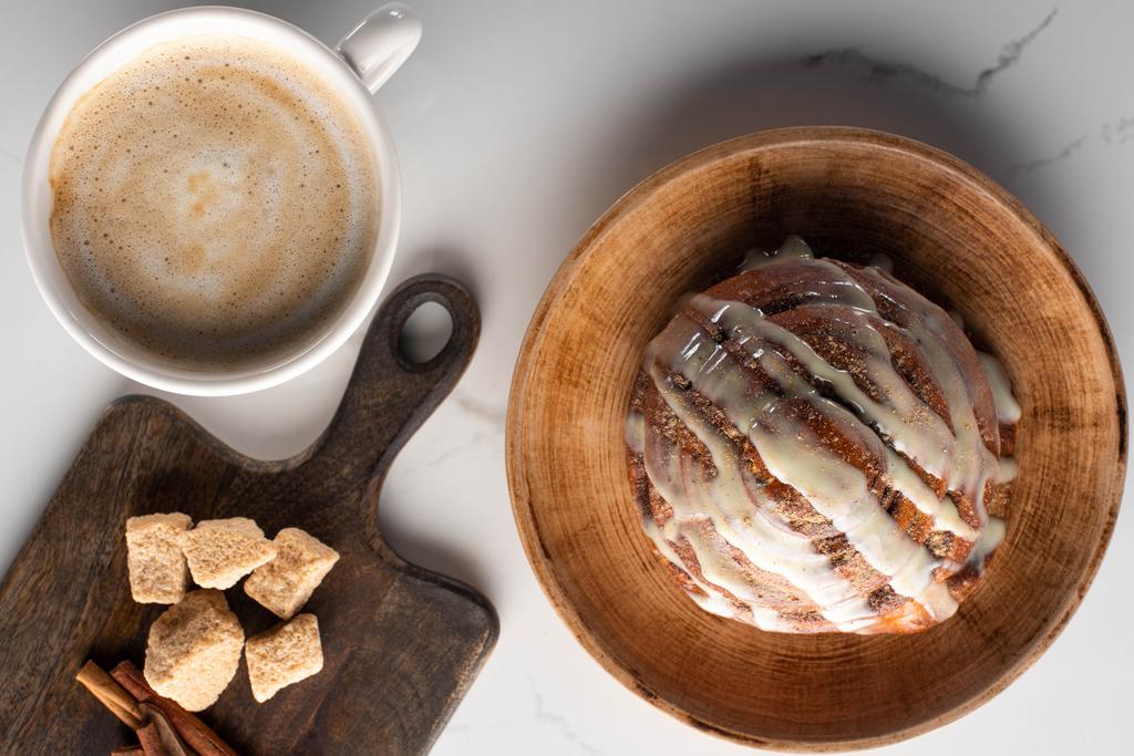 top view friss házi fahéjas tekercs tányéron márvány felületen vágódeszka barna cukorral, fahéjas pálcikák kávé mellett - Fotó, kép