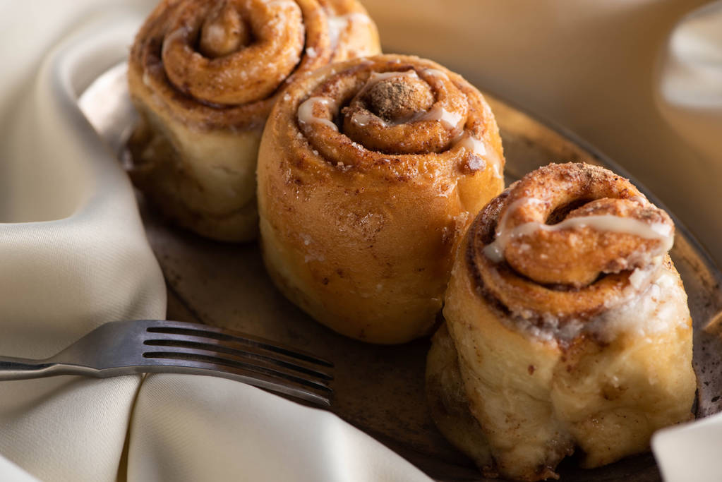 close up view of fresh homemade cinnamon rolls on board on satin cloth with fork - Photo, Image