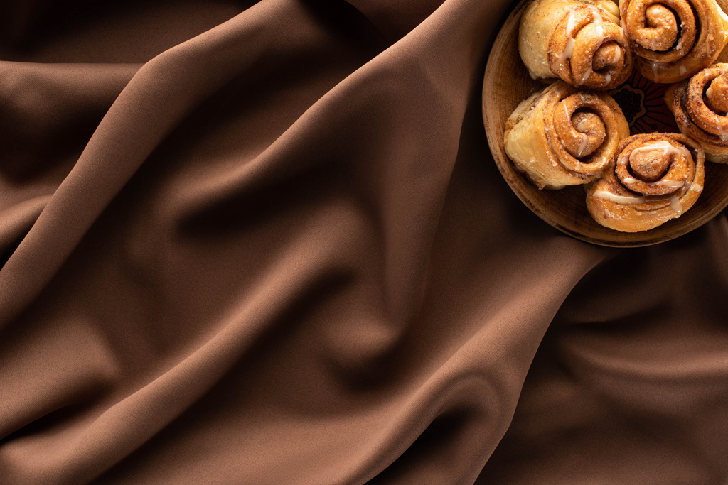 top view of fresh homemade cinnamon rolls on silk brown cloth - Photo, Image