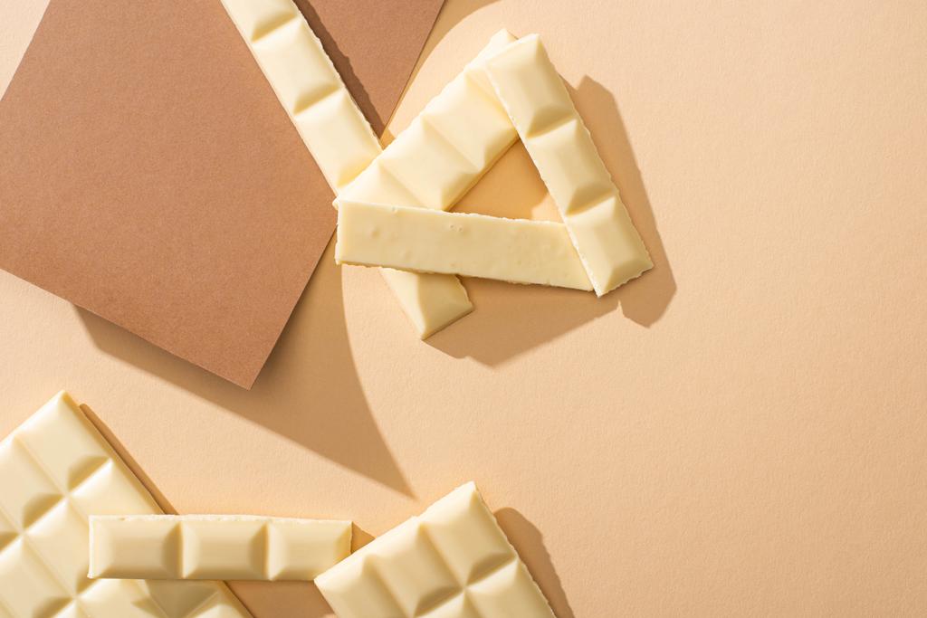 Bej arka planda kağıt üzerinde lezzetli beyaz çikolata parçalarının üst görünümü - Fotoğraf, Görsel