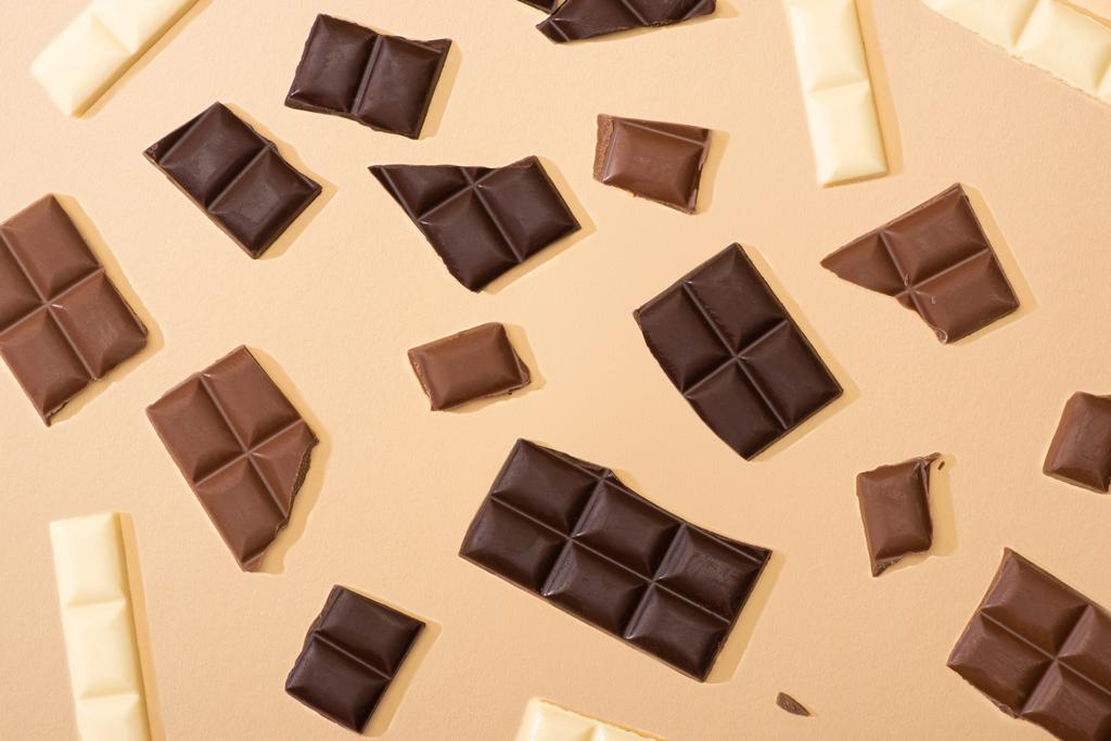 vista superior de deliciosos pedaços de chocolate escuro, leite e branco no fundo bege
 - Foto, Imagem
