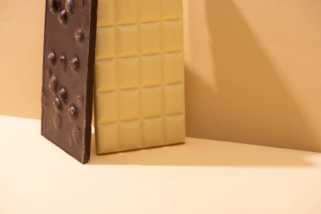 Bej arka planda fındıklı lezzetli beyaz ve siyah çikolatalar. - Fotoğraf, Görsel