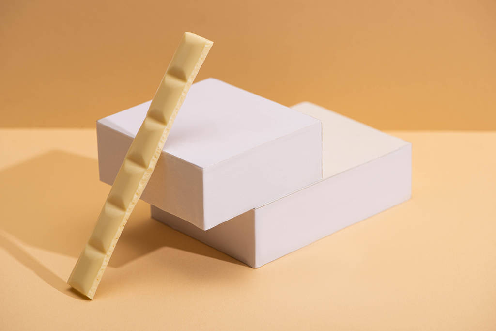 deliciosa pieza de chocolate blanco y cubos sobre fondo beige
 - Foto, Imagen