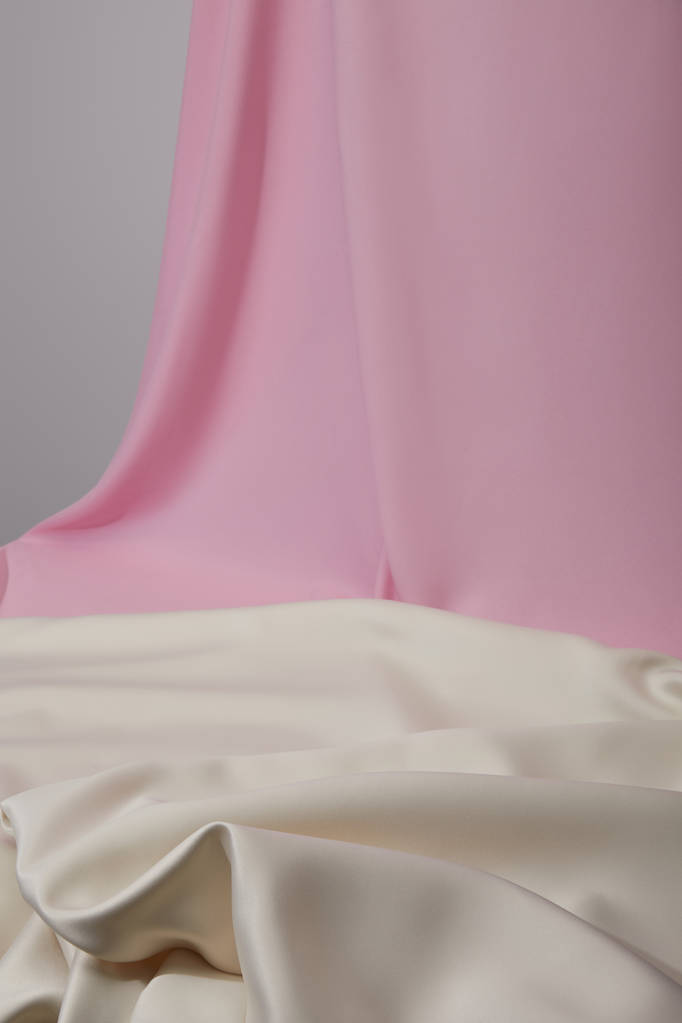 επιλεκτική εστίαση ροζ και λευκού μαλακού και κυματιστού υφάσματος που απομονώνεται σε γκρι - Φωτογραφία, εικόνα