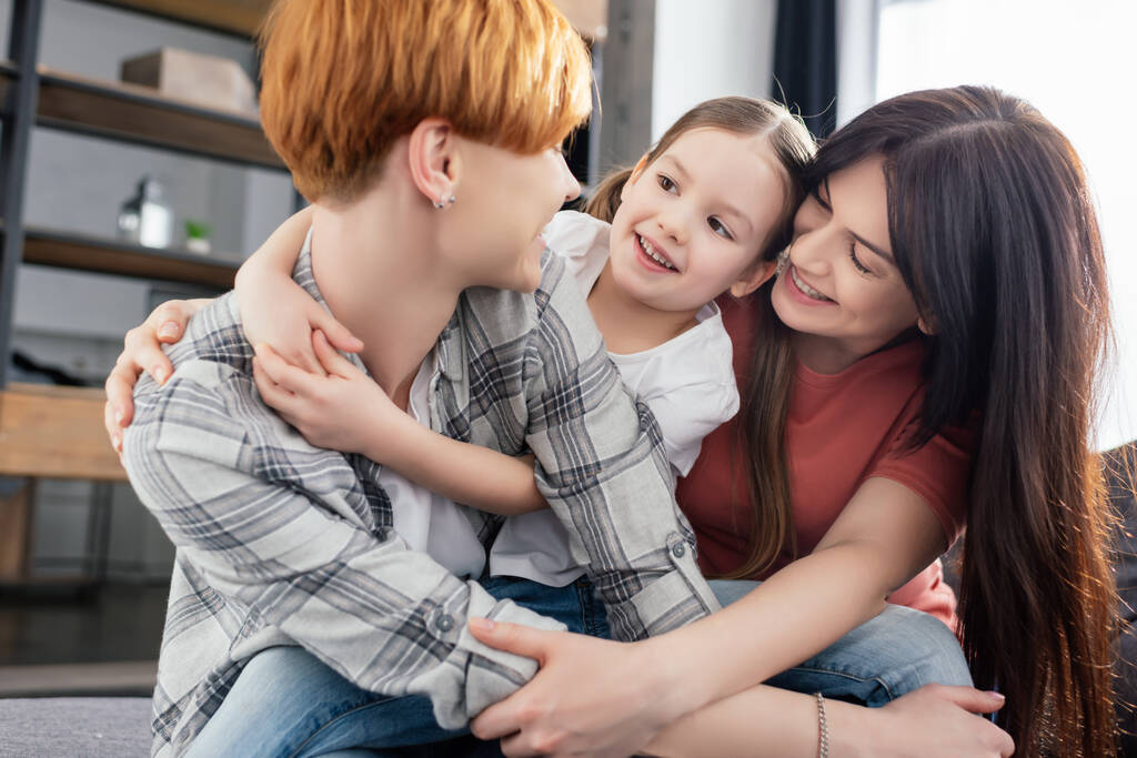 Cheerful same sex couple embracing daughter at home  - Photo, Image