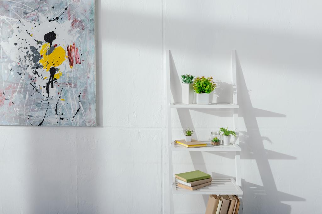 Art près des livres et des plantes sur l'étagère près du mur blanc avec lumière du soleil
 - Photo, image