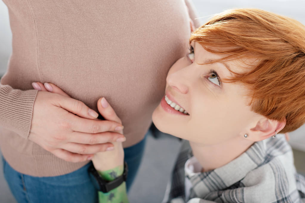 Mulher sorrindo de mãos dadas e tocando barriga de namorada grávida em fundo cinza
 - Foto, Imagem