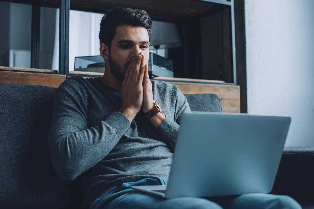 Shocked man with hands near mouth watching pornography on laptop in living room - Photo, Image