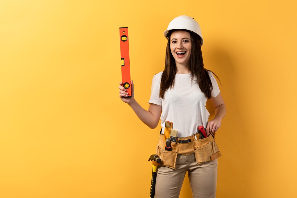 usmívající se údržbářka v helmě drží lihoviny na žlutém pozadí  - Fotografie, Obrázek