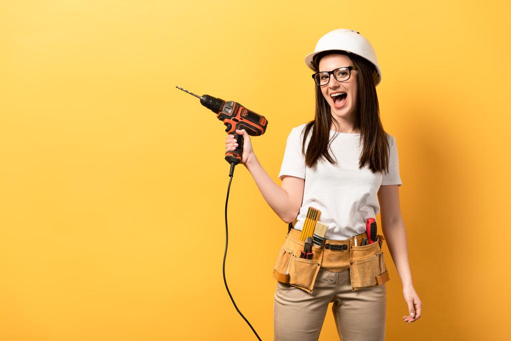 positive handywoman screaming and holding drill on yellow background  - Photo, Image