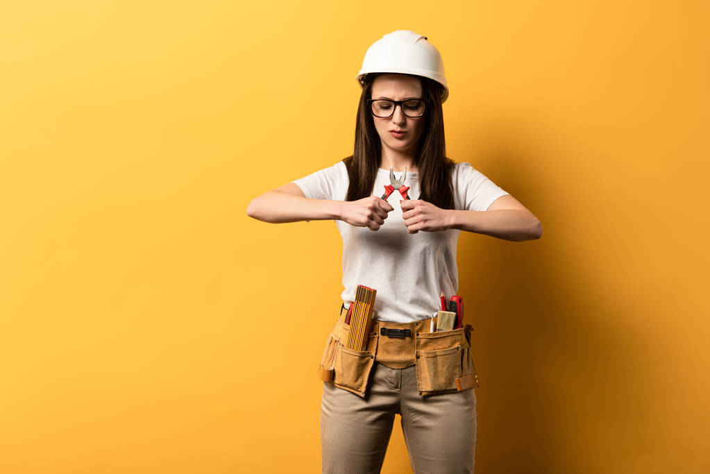 концентрированная работница в шлеме держит плоскогубцы на желтом фоне
  - Фото, изображение