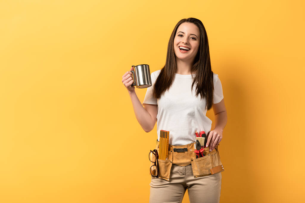 usmívající se údržbářka drží kovový pohár na žlutém pozadí  - Fotografie, Obrázek
