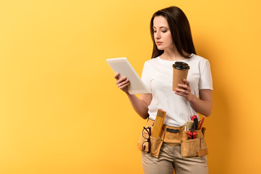 handige vrouw met behulp van digitale tablet en het houden van papieren beker op gele achtergrond  - Foto, afbeelding