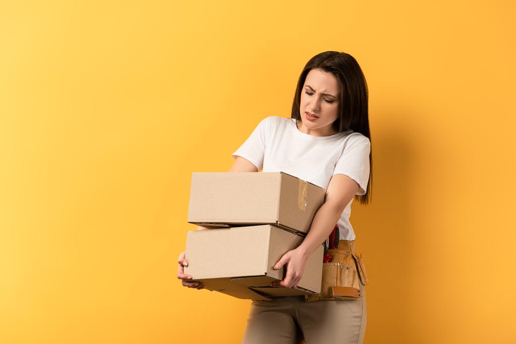 tired repairwoman holding carton boxes on yellow background  - Photo, Image
