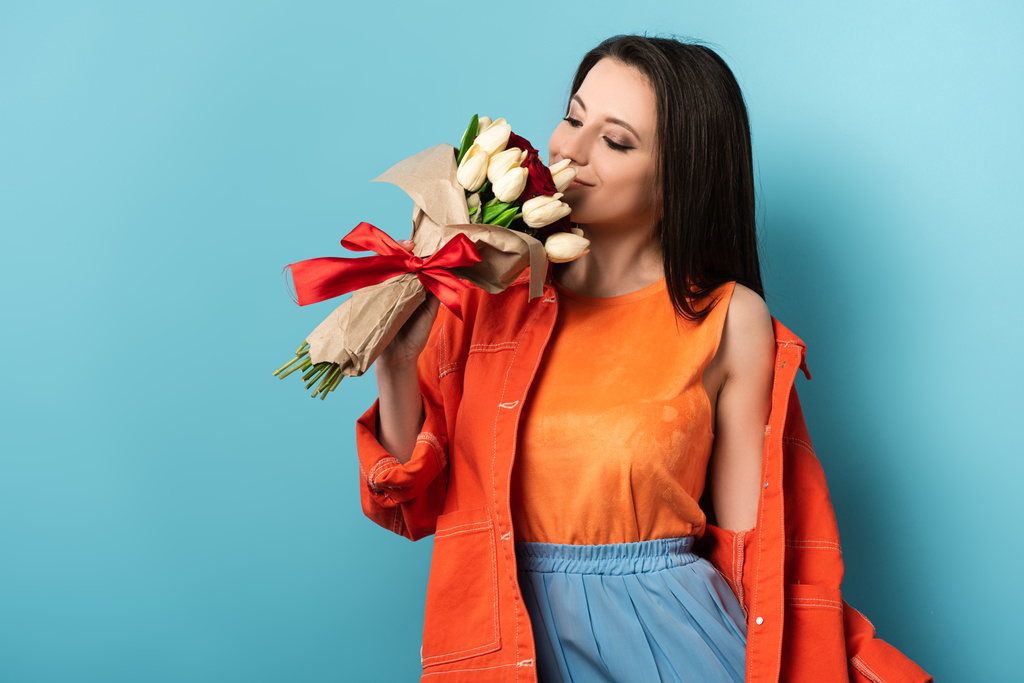 smiling woman in jacket smelling bouquet on blue background  - Photo, Image