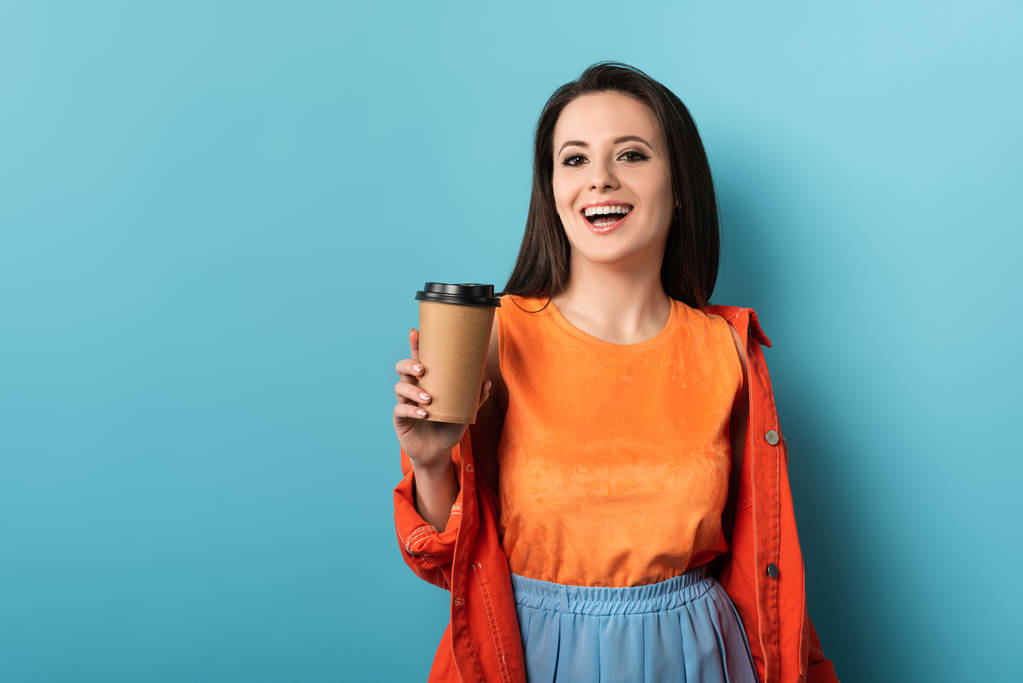 улыбающаяся женщина держит бумажную чашку с кофе на синем фоне
  - Фото, изображение