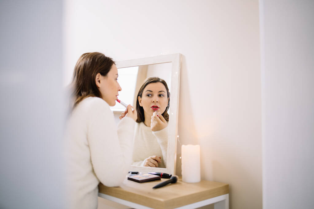 Kobieta nakładająca czerwoną szminkę przed lustrem - Zdjęcie, obraz