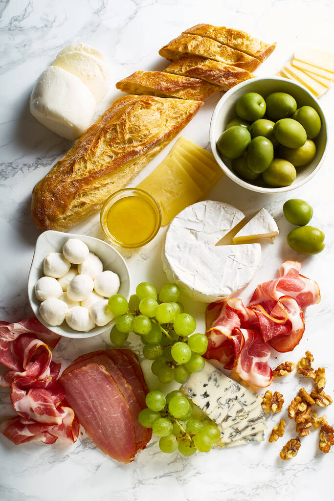 Сырная тарелка с мясом и фруктами с багетом и деликатесами на мраморной доске, концепция итальянской кухни
    - Фото, изображение