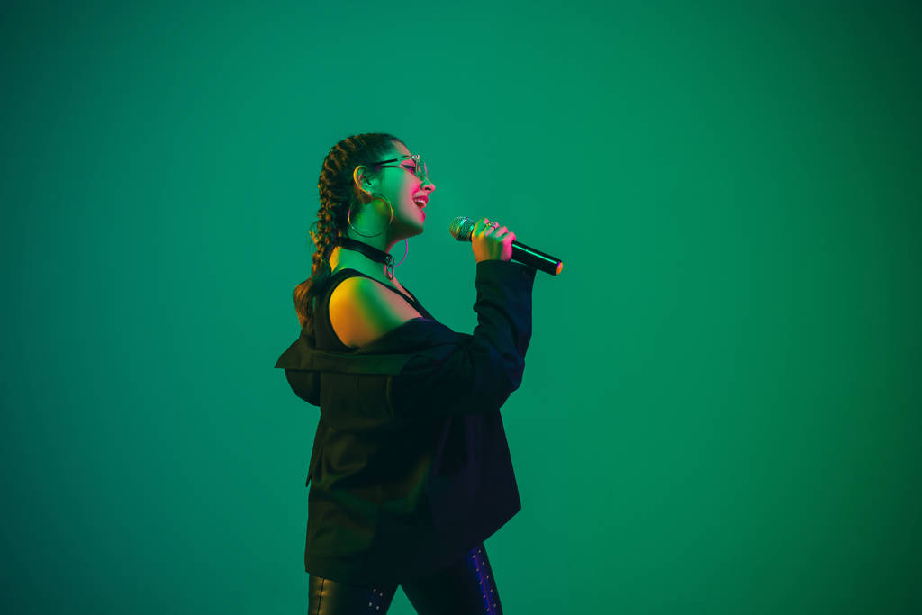 Caucasian female singer portrait isolated on green studio background in neon light - Fotó, kép