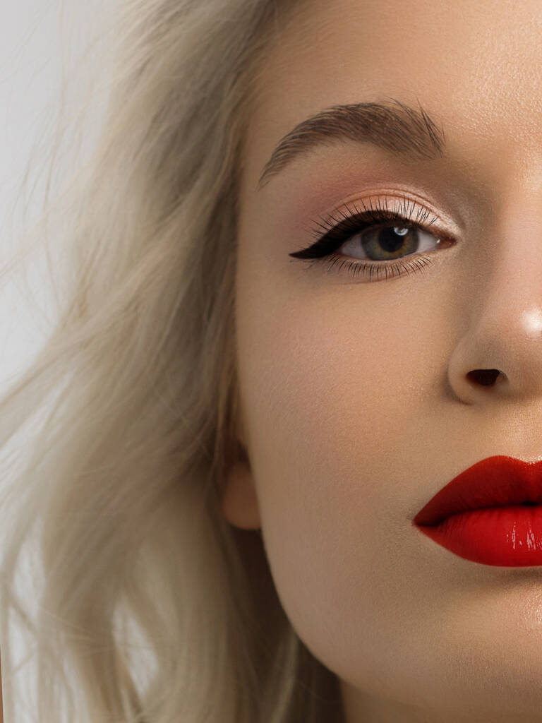 Close-up beauty of a half female face with creative fashion evening make-up. Black arrows on the eyes and extremely long eyelashes, on plump lips matte scarlet lip color. Well-groomed skin after spa - Photo, Image
