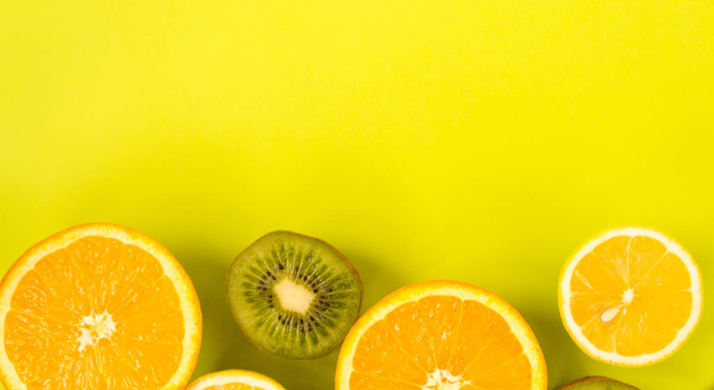 Een fruitframe. Kleurrijke verse citrusvruchten op een licht groene achtergrond. Sinaasappel, mandarijn, citroen en kiwi worden in tweeën gesneden. Platte lay, bovenaanzicht, kopieerruimte. Gezond eten concept. - Foto, afbeelding