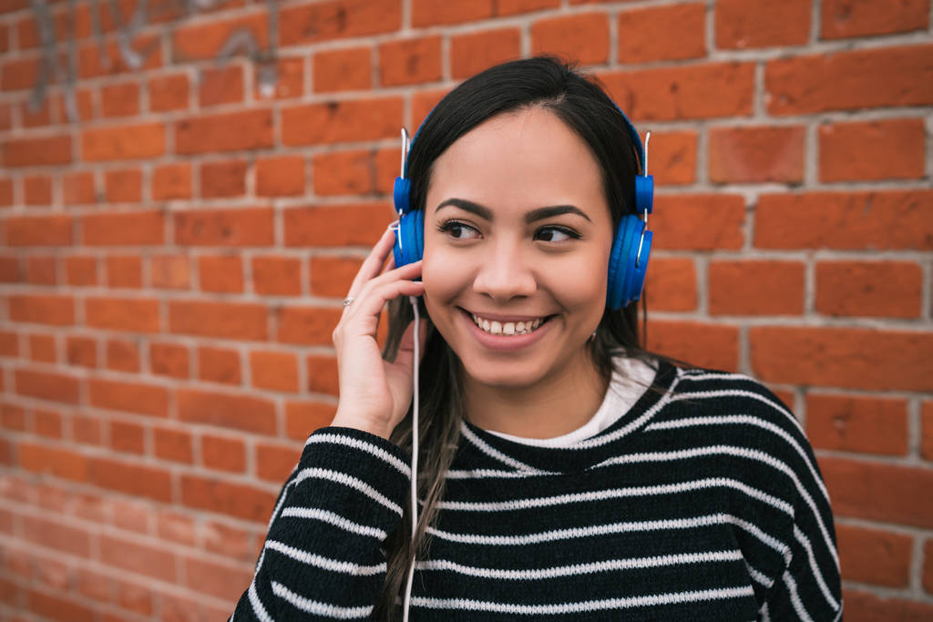 Retrato de una joven hermosa mujer escuchando música con auriculares azules en la calle. Al aire libre. - Foto, Imagen