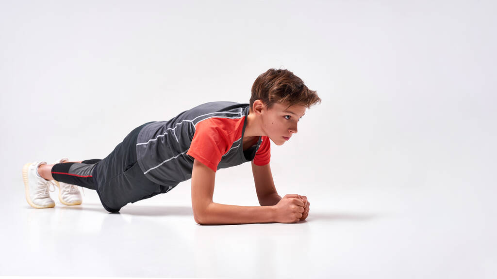 Βελτιώσου. Full-length πλάνο ενός έφηβου αγοριού που ασχολούνται με τον αθλητισμό, αναζητούν επικεντρώθηκε ενώ κάνει push-ups. Απομονωμένο σε λευκό φόντο. Εκπαίδευση, ενεργός τρόπος ζωής - Φωτογραφία, εικόνα