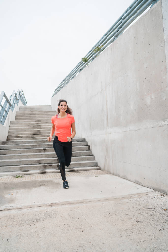 Retrato de una mujer de fitness corriendo por la calle sobre fondo gris. Deporte y estilo de vida saludable. - Foto, Imagen