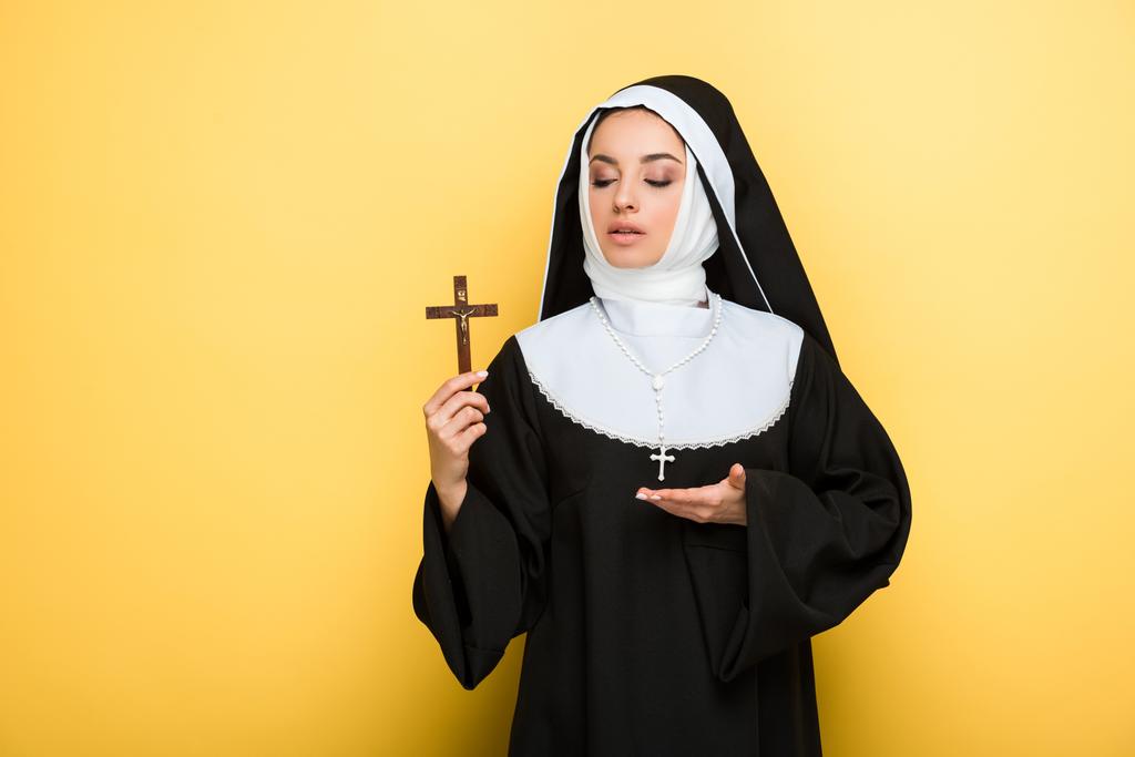 beautiful young nun showing cross on yellow - Photo, Image