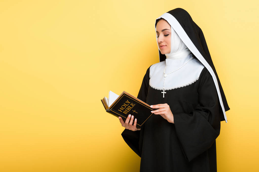 красивая улыбающаяся монахиня, читающая Святую Библию на сером
 - Фото, изображение