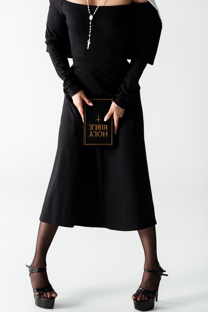bijgesneden weergave van sexy non in zwarte jurk houden bijbel op grijs - Foto, afbeelding