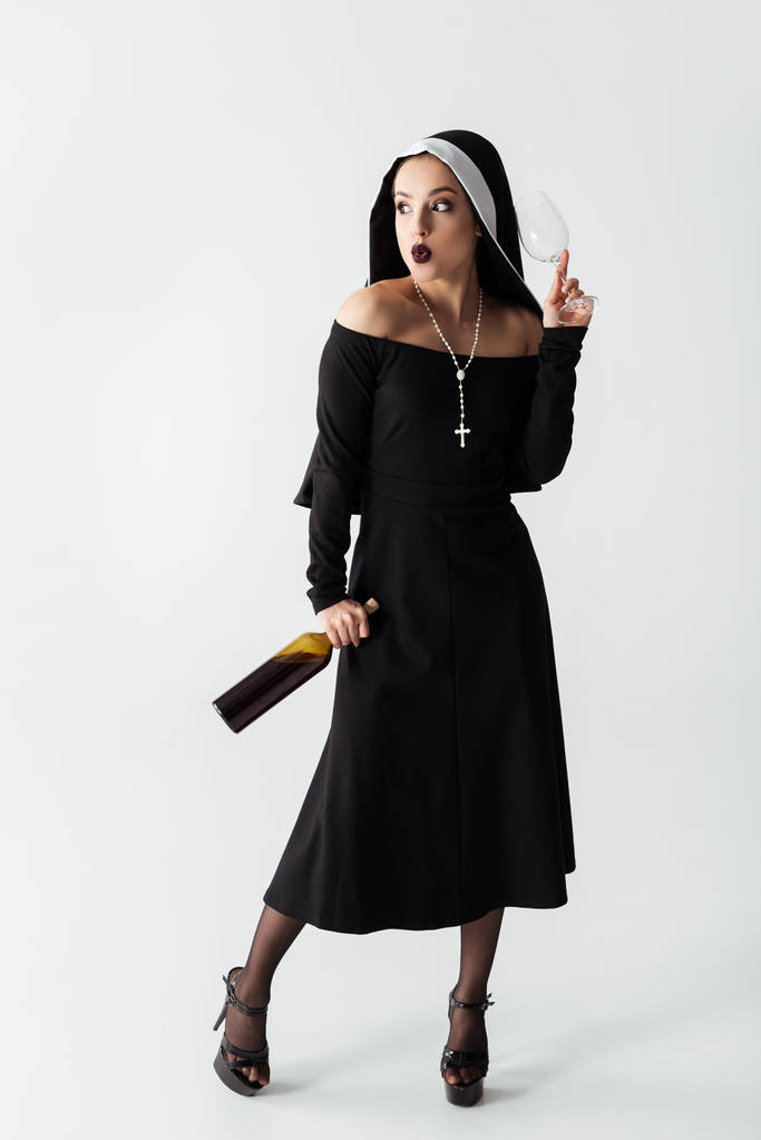 attractive sexy nun holding glass and bottle of wine on grey - Photo, Image