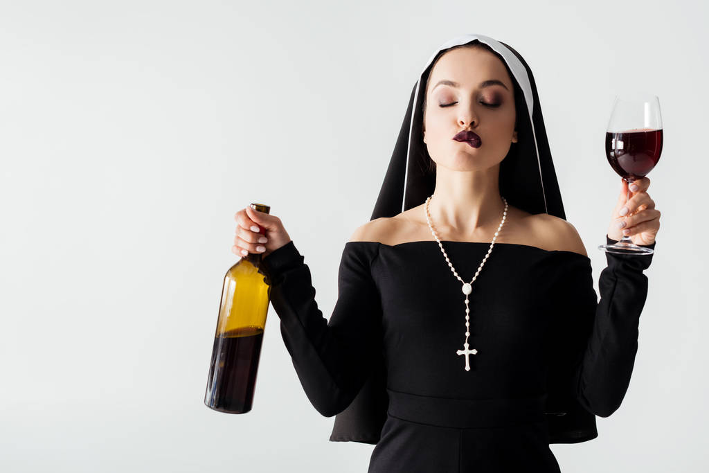 atrakcyjna seksowna zakonnica z zamkniętymi oczami gryząca wargę trzymając szklankę i butelkę wina odizolowaną na szaro - Zdjęcie, obraz
