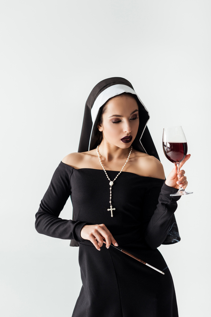 attractive nun holding glass of wine and cigarette in mouthpiece isolated on grey  - Photo, Image