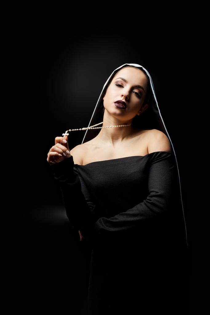 σέξι νεαρή καλόγρια με μαύρο φόρεμα κρατώντας σταυρό, απομονωμένη σε μαύρο   - Φωτογραφία, εικόνα
