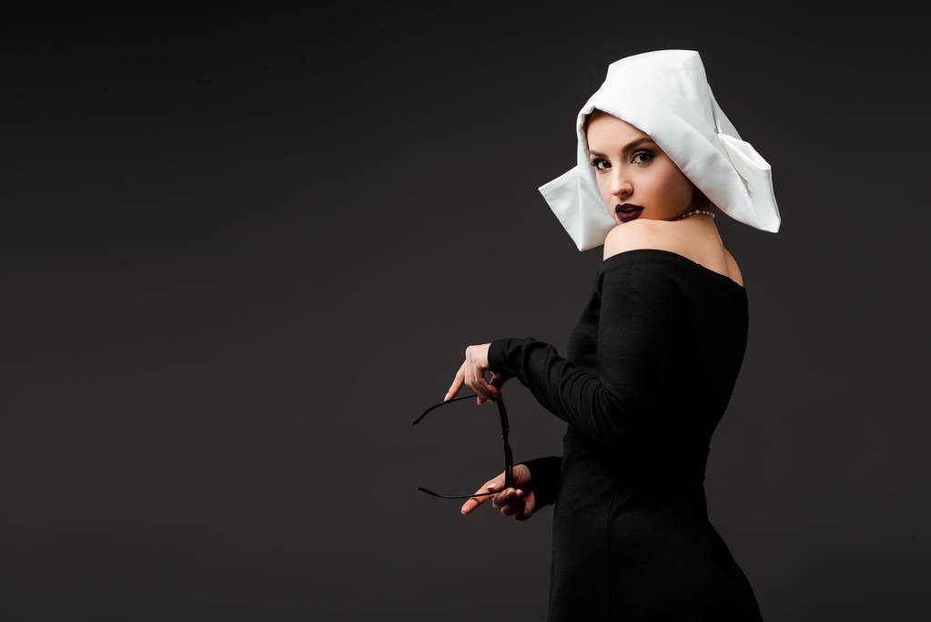 seksikäs nuori nunna musta mekko tilalla aurinkolasit, eristetty harmaa
   - Valokuva, kuva