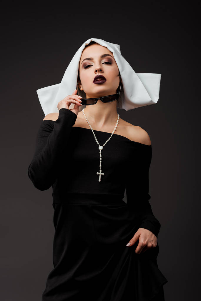 attractive sexy nun in black dress and sunglasses, isolated on grey - Photo, Image