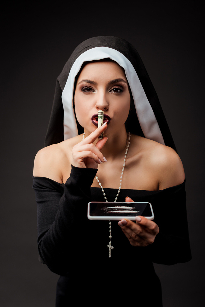 Emotionale sexy Nonne mit Dollar-Banknote und Smartphone mit Kokainlinien, die das Schweigesymbol isoliert auf grau zeigen - Foto, Bild
