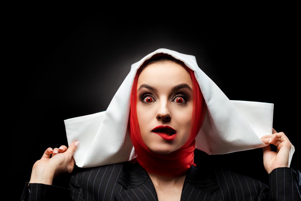 привлекательная сексуальная демоническая монахиня с красными глазами кусающими губы изолированными от черного
 - Фото, изображение