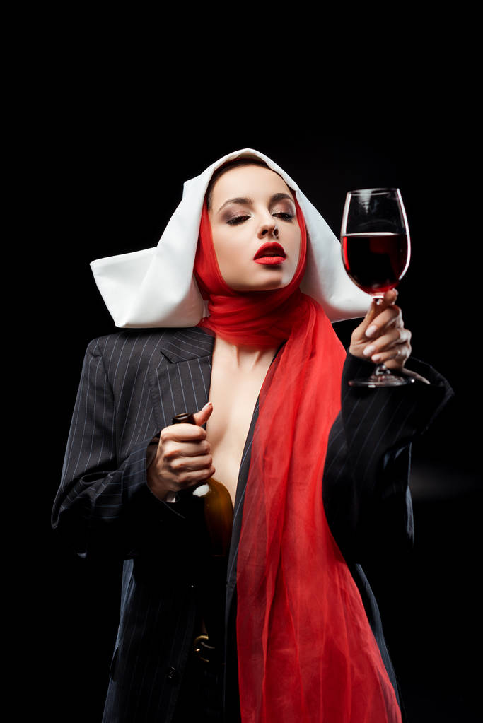 чувственная монахиня держит стакан и бутылку красного вина изолированы на черном
 - Фото, изображение