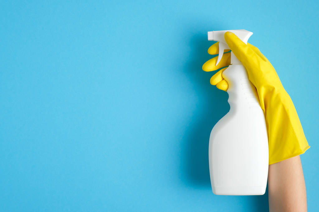 Hand in een gele rubberen handschoen houdt schonere spray fles over blauwe achtergrond. Schoonmaakservice banner model. Huisvesting en huishouding concept. Vlakke lay, bovenaanzicht - Foto, afbeelding