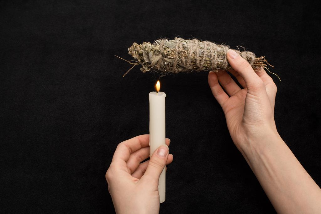 Widok upraw szamana trzymającego ziołowy kij rozmazany powyżej palącej się świecy odizolowanej na czarno  - Zdjęcie, obraz